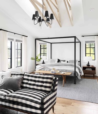 Bedroom with canopy bed, black and white checked sofa, bench, chandelier, nightstand, lamp.