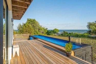 A view off of a wood deck with a shipping container pool out front.