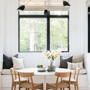Banquette seating in kitchen with white round table, wood dining chairs, modern chandelier.
