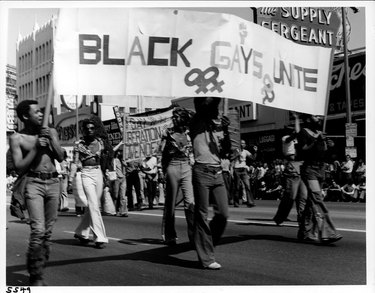 Men hold a "Black Gays Unite" banner at the Los Angeles Christopher Street West pride parade. 1975.