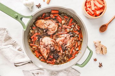 Simmering chicken, vegetables, and liquids in a green skillet