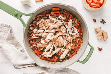 Chicken on top of vegetable mixture in a green skillet