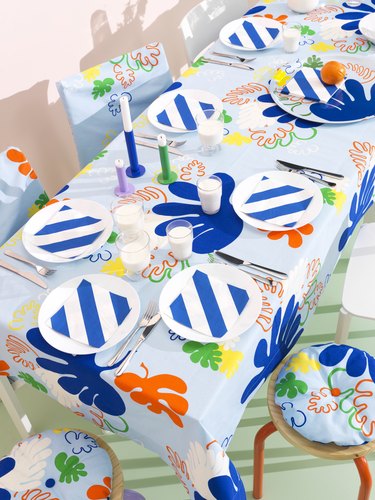 An IKEA table setting featuring a colorful floral tablecloth and white plates topped with blue and white striped napkins.