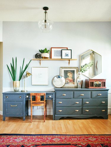 eclectic home office with blue desk that extends to a matching dresser, with a red rug and art surrounding the desk