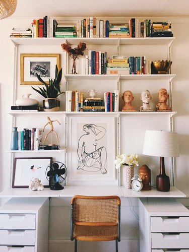 white modern home office with built-in shelving system around the desk, styled with books, sculptures and art