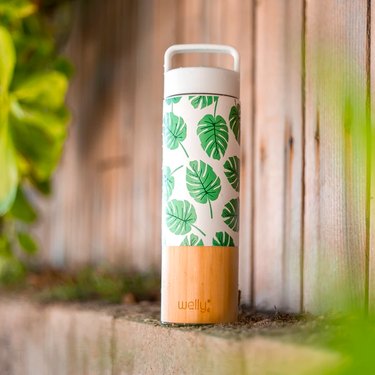 A travel mug with a wooden base and white and monstera-print body.