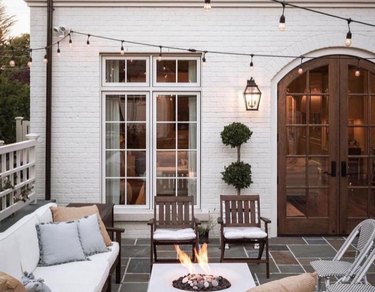 Patio with couch and chairs, firepit, white lights.