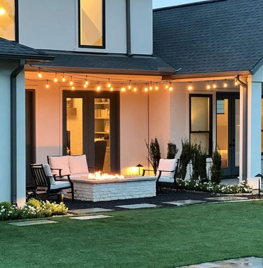 Patio with chairs and love seat, firepit, white lights, lawn.