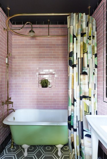 retro bathroom with pink subway tile, green clawfoot bathtub and geometric hex patterned black and white penny tile floor