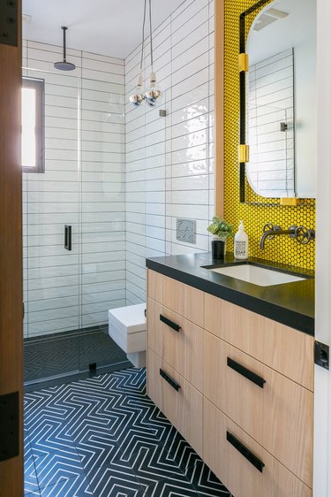 contemporary bathroom with yellow penny tile backsplash, geometric black and white tile floor, wood vanity adn white tile shower