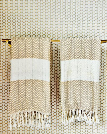 bathroom detail of white penny tile with sand colored grout and hanging boho tasseled towels