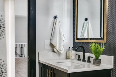 black, white and gold bathroom with black penny tile backsplash