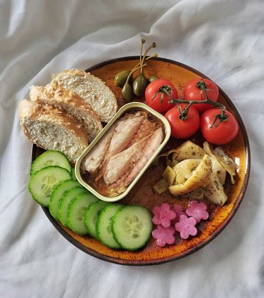 Tinned fish on a plate with bread, tomatoes, olives, and cucumbers