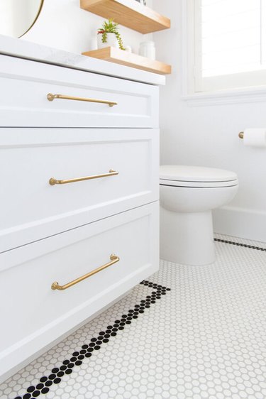 white bathroom with gold accents and white penny tile floor with black border