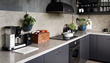 Kitchen with charcoal gray cabinets, concrete backsplash and counter, black appliances.