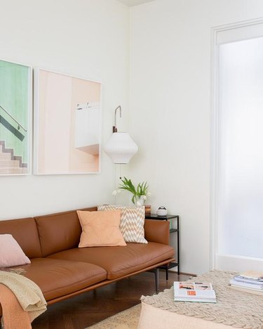 living room with brown leather sofa and peach pillow, wall art, and ottoman