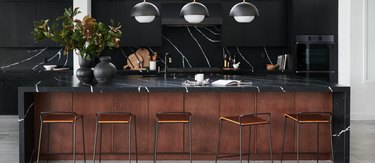 Kitchen with black cabinets, walnut island, black marble counters, black appliances.