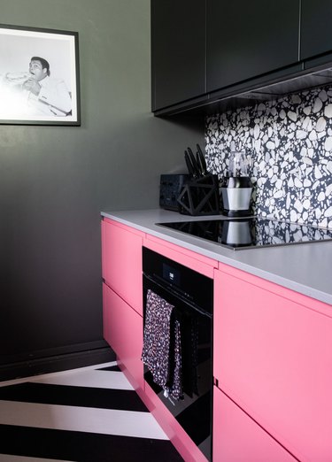 Kitchen with hot pink and black cabinets, black and white marble backsplash, black appliances.