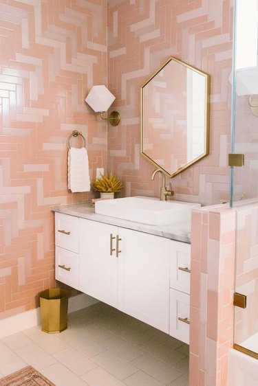 midcentury bathroom with pink mosaic tiles, white floating vanity and brass accents, and hex mirror