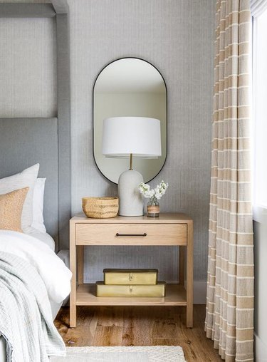 Bedroom with gray walls, a grey fabric headboard and tan curtains.