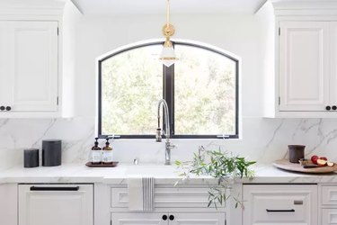 all white kitchen with window over the sink and marble countertops