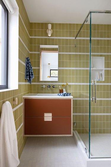 midcentury bathroom with avocado green wall tiles, rust floating vanity, and large glass-walled shower
