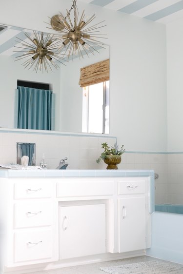midcentury bathroom with period vintage blue and white tiles, atomic chandelier, and linoleum floors