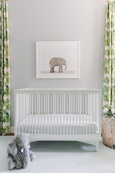 Nursery with gray walls, green patterned curtains and a white crib.