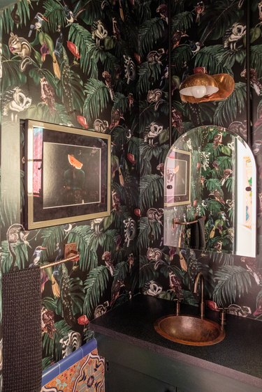 dark powder room with  jungle-themed wallpaper and copper sink