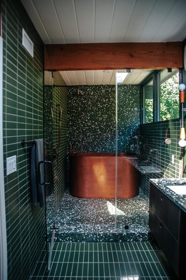 midcentury and contemporary bathroom with copper bathtub, tarrazzo tiles, and stacked horizontal tiles in forest green