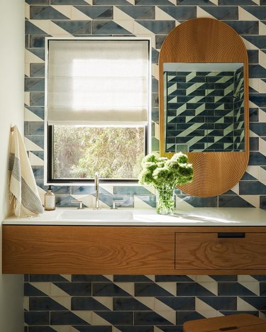 midcentury bathroom with blue and white geometric linear tile wall, brass pill-shaped mirror, and floating wood vanity