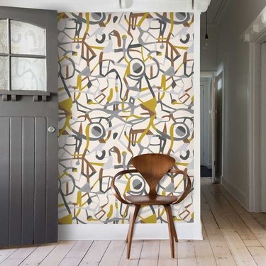 Entryway with modern wallpaper, wood floors, modern chair, gray door.