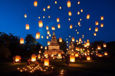 Sky lanterns ascending over a temple into the night sky.