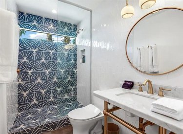 midcentury bathroom with blue starburst hex tiles, circle mirror, and glass shower wall
