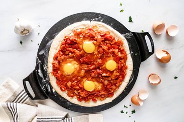 Pizza crust on a cast iron dish with tomato sauce and eggs
