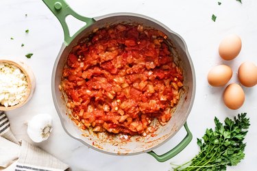 Green pan with diced tomato mixture on a white background