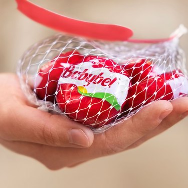 A hand holding a bag of Babybel cheese in its red casings.