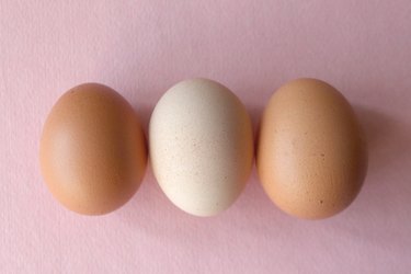 two brown eggs and one white egg over pink background