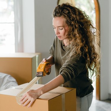 woman closing brown moving box with tape