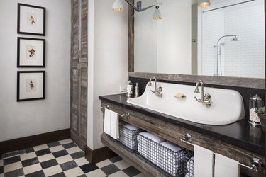Modern farmhouse bathroom idea with white trough sink, distressed wood vanity and acent wall, and black and white checkerboard floor