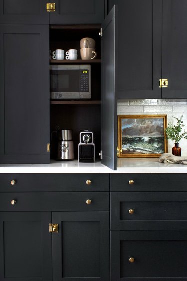 modern black kitchen with appliance garage housing espresso machine, milk frother, toaster, small microwave and blender.