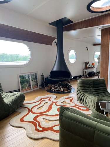 A living room with a fireplace, green seating, and a blobby rug on the ground