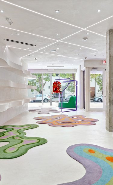 A large white showroom with brightly colored, swirly, blob-shaped rugs on the ground