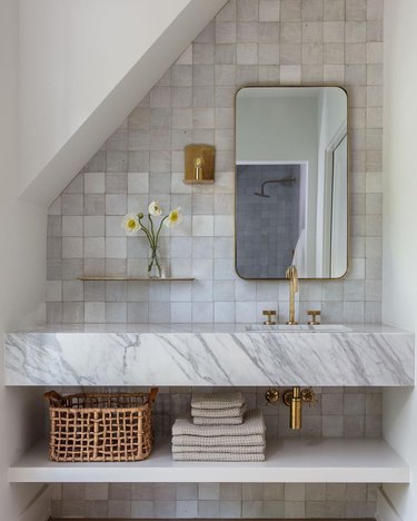 modern traditional bathroom with grayish white zellige tile backsplash, white marble counter and brass hardware and accents