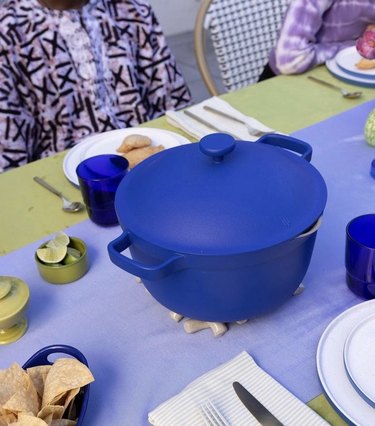 A blue Perfect Pot on a table with a light blue and green tablecloth. There are tortilla chips and a small green bowl of limes along with table settings.