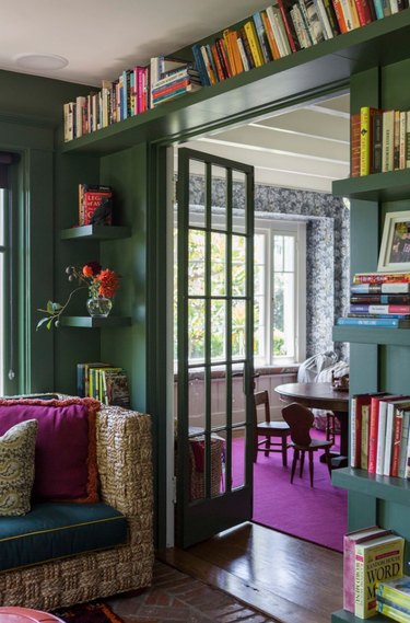 Living room with magenta rug, forest green walls, bookshelves.