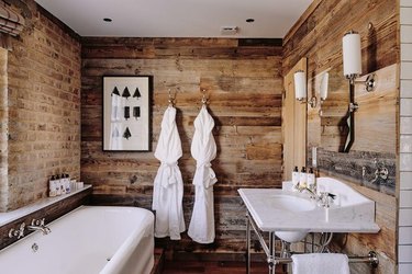 Bathroom with white tub and sink, reclaimed wood shiplap, brick wall.