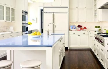 A modern kitchen with white cabinets, dark wood flooring, and blue lavastone countertops