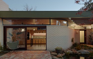 A modern cream brick house has a flat green metal roof and glass sliding doors.