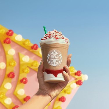 person holding frappuccino near colorful sign with light bulbs